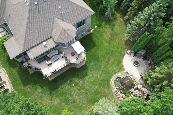 Aerial view of a large wooden deck with outdoor furniture, overlooking a grassy backyard with a water feature. - 36131 Pr 303 Road, Steinbach