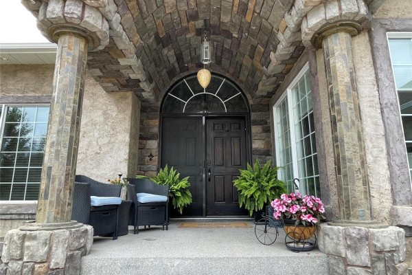 Front entrance of the house featuring large stone columns, arched stone detailing, and dark wood double doors. - 36131 Pr 303 Road, Steinbach