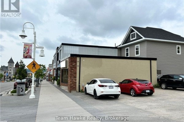 Rear view of a commercial building with tan siding, brick facade, and parked cars. - 361&365 King Street, Midland