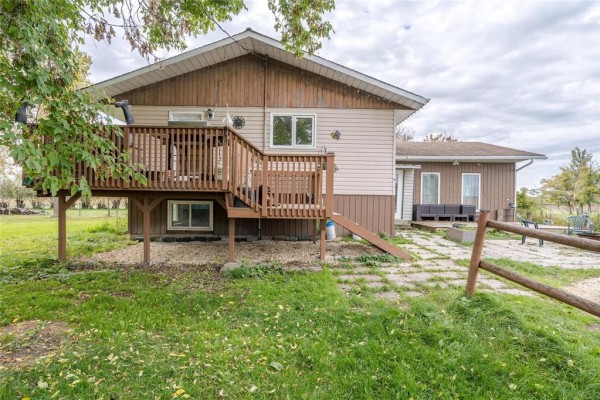 Side exterior view of a beige and brown house with a wooden deck and a stone patio in a grassy yard. - 36137 7n Road, Vita