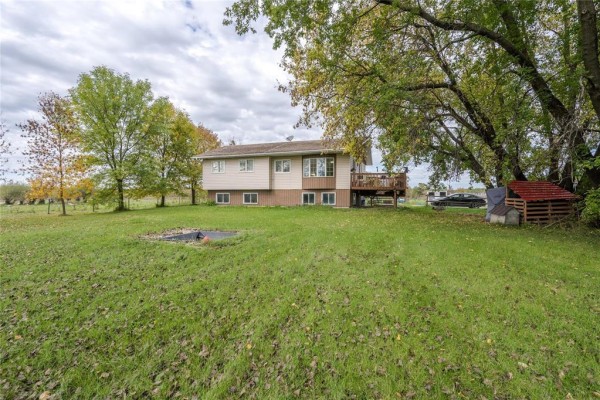 Wide view of the house from the backyard, with trees, grass, and a small red structure on the right. - 36137 7n Road, Vita