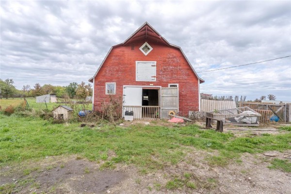 Front view of a weathered red barn with large double doors and small windows, surrounded by grass and debris. - 36137 7n Road, Vita