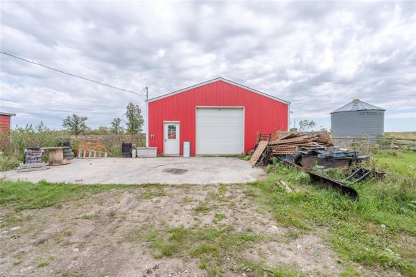 Front view of a bright red detached garage with a white roll-up door and a separate door, next to a silo. - 36137 7n Road, Vita