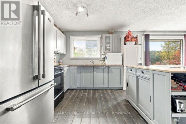 A kitchen with light grey cabinets, stainless steel refrigerator, black gas stove, and dark grey wood-look floors. - 36148 Highway 17 Highway, Laurentian Hills