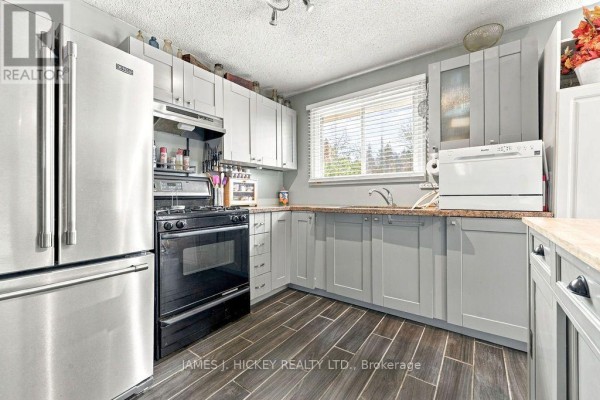 A kitchen with light grey cabinets, stainless steel refrigerator, black gas stove, and dark grey wood-look floors. - 36148 Highway 17 Highway, Laurentian Hills
