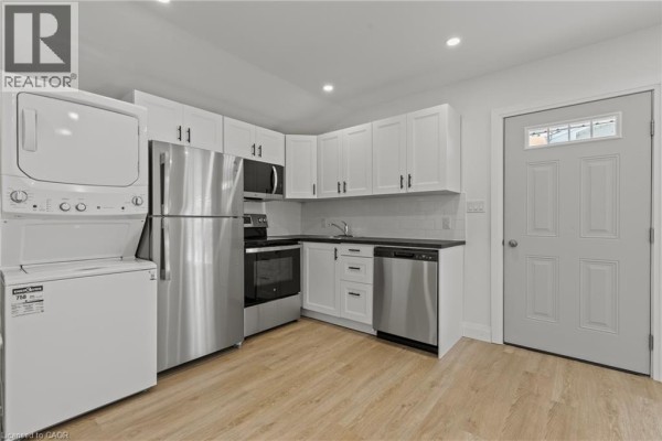 Kitchen and laundry area with white cabinets, stainless steel appliances, and a stacked washer and dryer. - 362 Gatfield Avenue Unit# 2, Welland