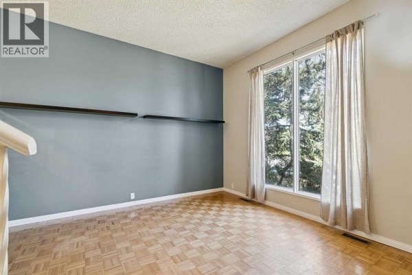 Empty room with large window, beige curtains, and gray accent wall with two shelves. - 3624 Cedarille Drive Sw, Calgary