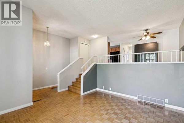 Living room and kitchen area with wood parquet flooring and an open railing overlooking the kitchen. - 3624 Cedarille Drive Sw, Calgary