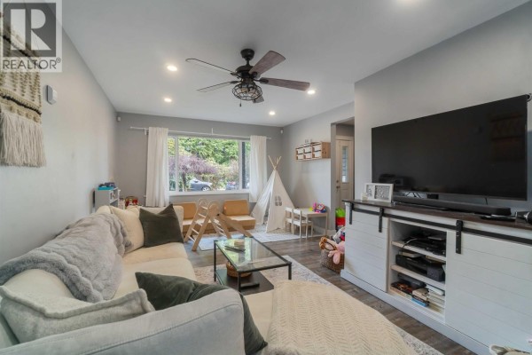 Living room with a sectional sofa, large TV, fireplace, and a window view of trees. - 3629-3631 Flint Street, Port Coquitlam