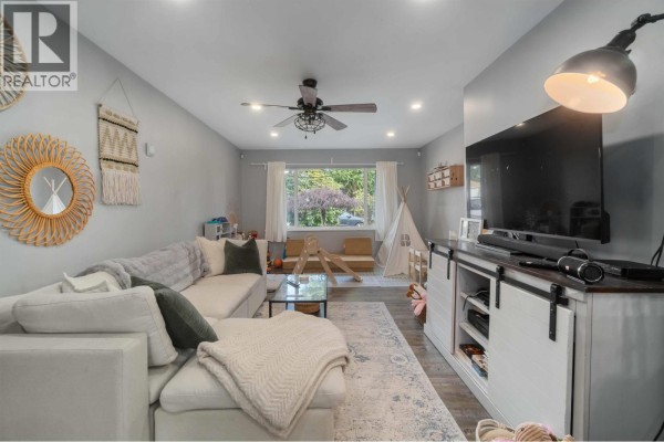 Living room with a white sectional sofa, large TV on a barn door cabinet, and ceiling fan. - 3629-3631 Flint Street, Port Coquitlam