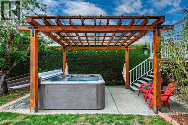 Backyard with a wooden pergola covering a grey hot tub, and two red chairs. - 3630 Waterhouse St, Port Alberni