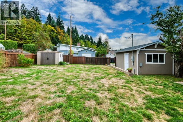View of a grassy backyard with two storage sheds and a fence. - 3630 Waterhouse St, Port Alberni