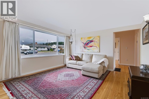 Living room with a cream sectional sofa, large window, and oriental rug. - 3630 Waterhouse St, Port Alberni