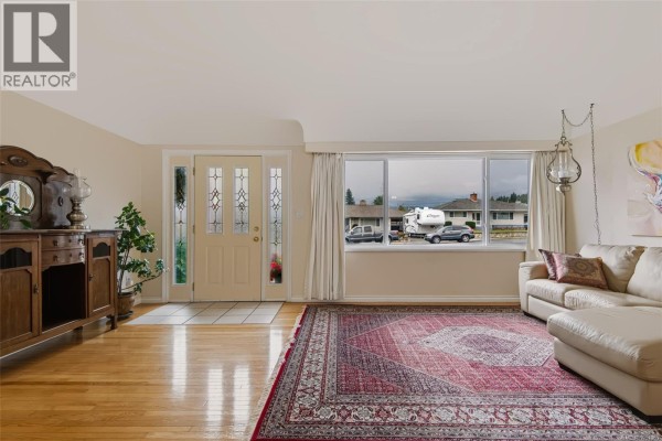 Entrance foyer and living room with a cream sofa, large window, and wooden floor. - 3630 Waterhouse St, Port Alberni