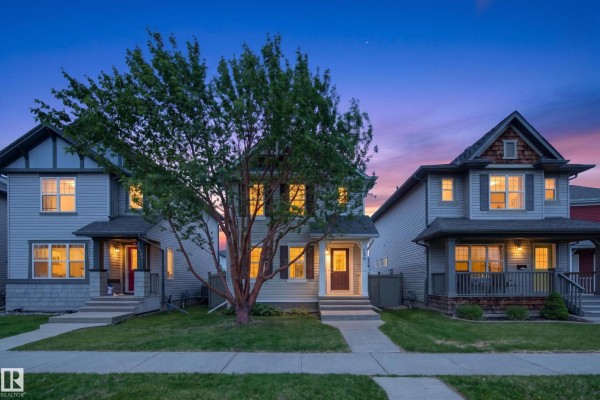 Front exterior of a beige townhouse at dusk with interior lights on. - 3634 12 St Nw, Edmonton