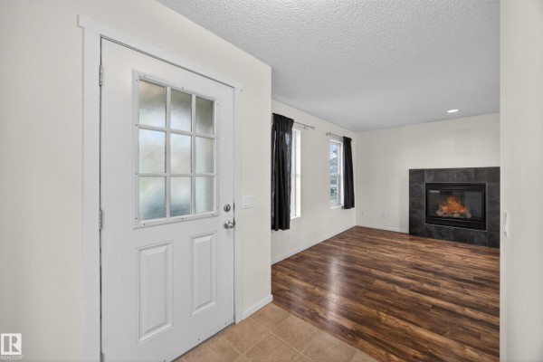 View of the entryway showing a white door, tiled floor, and living room with fireplace. - 3634 12 St Nw, Edmonton
