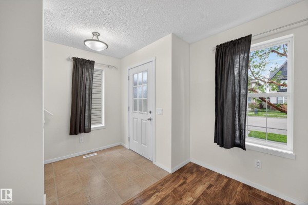Entryway with tiled floor, white door, and wood-look flooring in adjacent room. - 3634 12 St Nw, Edmonton