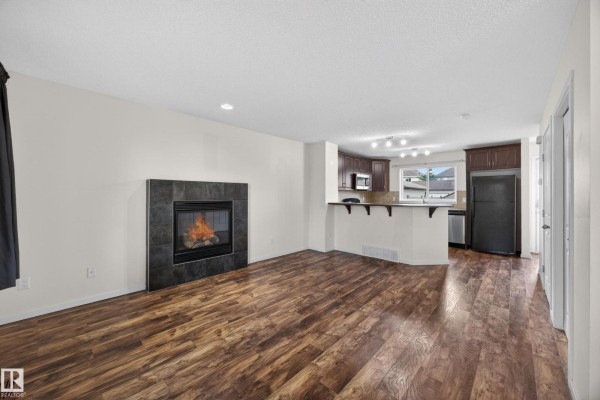 Living room with wood-look flooring, fireplace, and open-concept kitchen area. - 3634 12 St Nw, Edmonton
