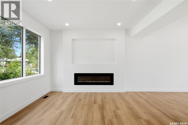 Interior hallway with white walls, light wood laminate flooring, and a staircase to the right. - 3638 Argyle Road, Regina
