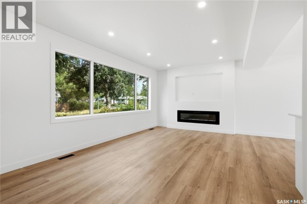 Living room with a large window, white walls, and a modern electric fireplace. - 3638 Argyle Road, Regina