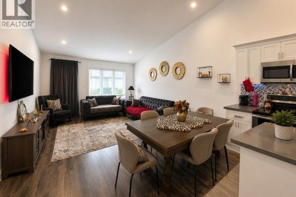 Living and dining area with vaulted ceilings, dark grey and red tufted sofas, and a wooden dining table. - 3639 Hallee, Windsor