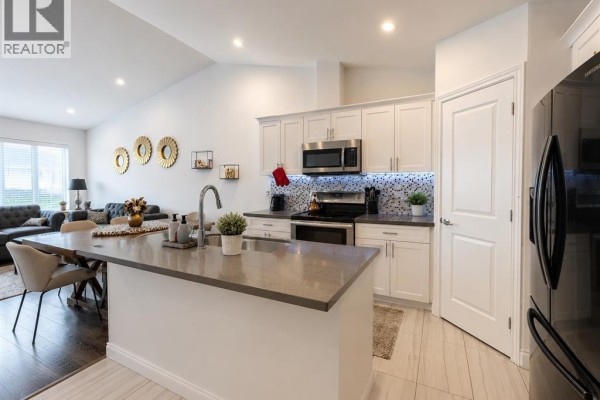 Modern kitchen with white cabinets, stainless steel appliances, a grey island with a sink, and adjacent dining area. - 3639 Hallee, Windsor