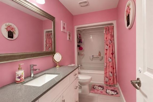 Pink bathroom with a granite countertop vanity, large mirror, toilet, and a white bathtub with a Hello Kitty shower curtain. - 3639 Hallee, Windsor