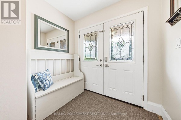 Interior foyer with double glass doors, bench seating, and a framed mirror on the wall. - 364 Fennell Avenue W, Hamilton