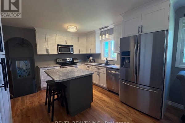 Kitchen with white cabinets, granite island with stools, and stainless steel refrigerator. - 364 Genier Road, Cochrane
