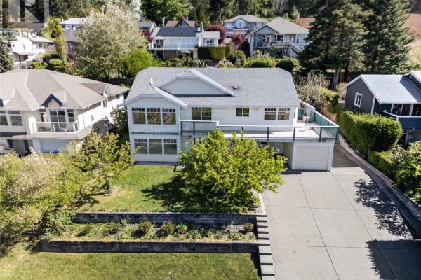 Aerial view of a white two-story house with a deck, garage, and surrounding neighborhood. - 365 Panorama Cres, Courtenay