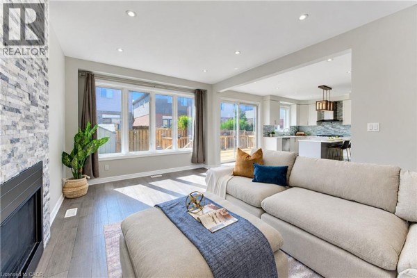 Living room with stone fireplace, large window overlooking backyard, and view into kitchen. - 365 Woolwich Street, Waterloo