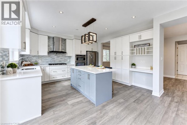Modern kitchen with white cabinets, grey island, stainless steel appliances, and built-in desk. - 365 Woolwich Street, Waterloo