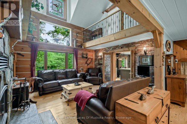 Living room with vaulted ceiling, exposed beams, stone fireplace, leather furniture, and loft overlook. - 3650 Muskoka Road 117, Lake Of Bays