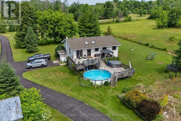 Aerial view of the rear of a house featuring a wooden deck with a pool and hot tub. - 3656 County 14 Road, Stone Mills