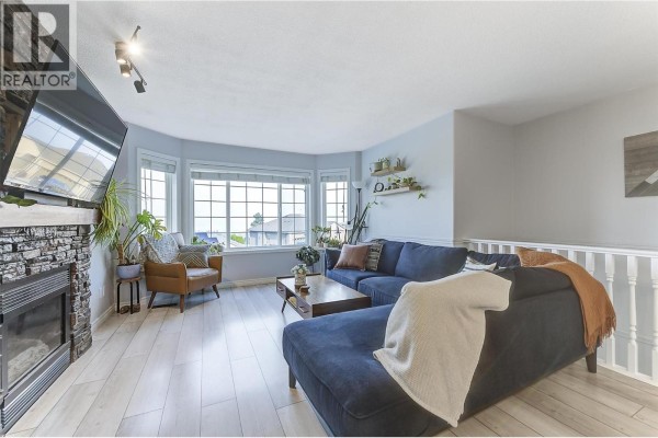 View of the living room from the right, showing a dark blue sectional, a coffee table, and bay windows. - 3656 Walnut Glen Drive, West Kelowna