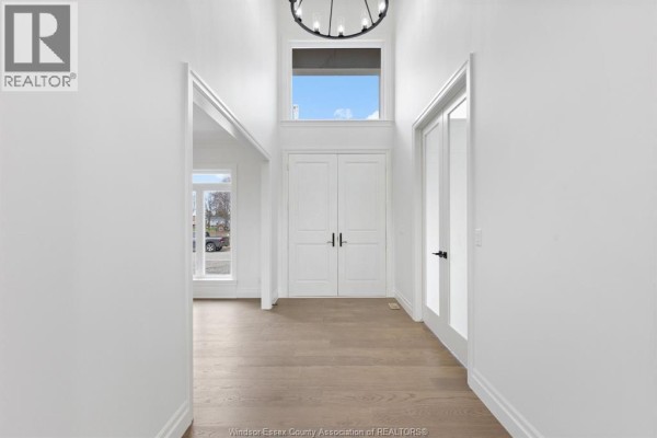 Foyer with double white doors, a chandelier, and light hardwood floors leading to a large window. - 3657 Oakridge Avenue, Windsor