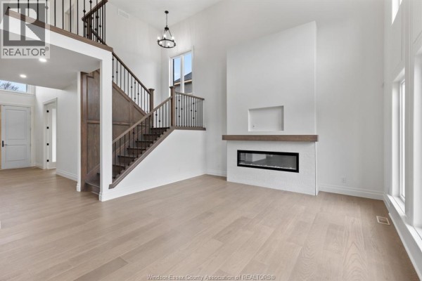 Living room with a two-story ceiling, dark wood staircase, modern fireplace, and large windows. - 3657 Oakridge Avenue, Windsor
