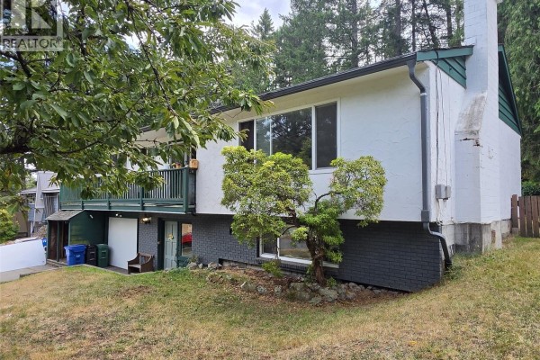 Side view of the house showing the stucco exterior, green trim, and a large chimney. - 3657 Sunrise Pl, Nanaimo