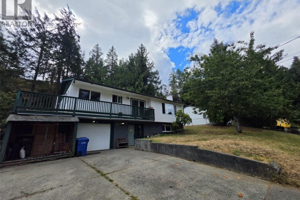 Wide angle of the property showcasing the house, driveway, and surrounding trees under a cloudy sky. - 3657 Sunrise Pl, Nanaimo
