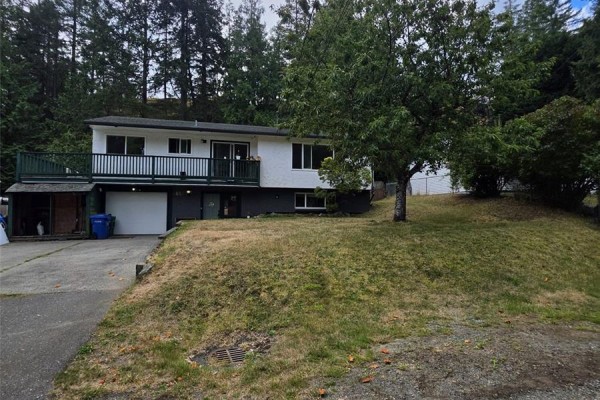 Exterior of the split-level home with a sloped lawn and mature trees in the background. - 3657 Sunrise Pl, Nanaimo