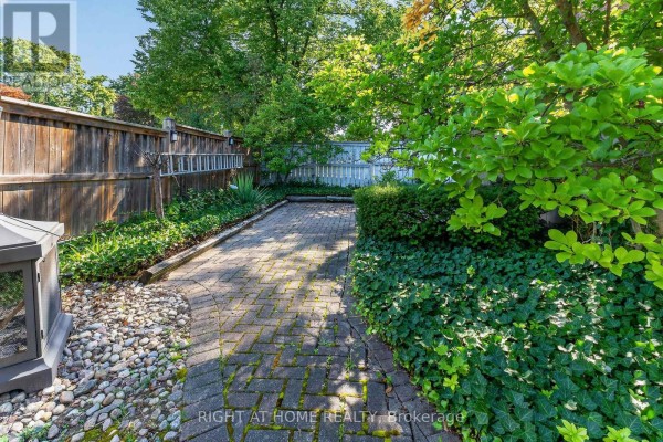Brick pathway and lush greenery in backyard with outdoor fireplace - 366 Burlington Crescent London South