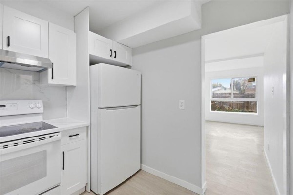White kitchen with stainless steel appliances and view into a living area. - 366 Houde Drive, Winnipeg
