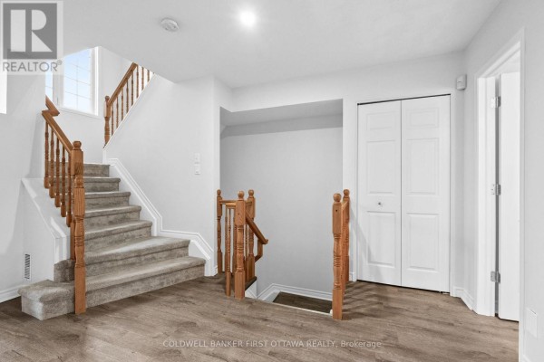 Hallway landing with carpeted stairs, wood railings, and white bi-fold doors. - 366 Wiffen Private, Ottawa