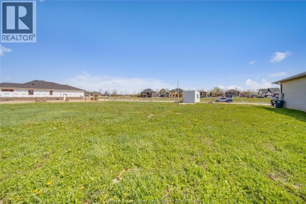 Wide view of a vacant lot with green grass and some construction materials, houses and a utility box in background. - 3667 Farrow Avenue, Windsor