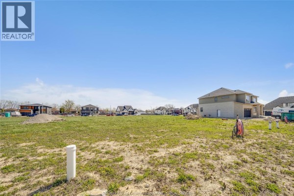 Unfinished lot with short grass and white pipes, featuring houses under construction and completed homes in the background. - 3667 Farrow Avenue, Windsor