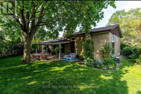 View of the house's rear brick exterior, backyard patio, and expansive green lawn with trees. - 3668 The Credit Woodlands Road, Mississauga