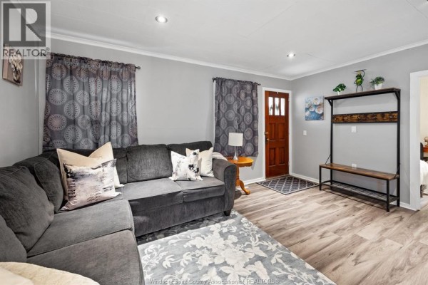 Living room with a dark grey sectional sofa, floral rug, and wood floor. - 3672 Girardot, Windsor
