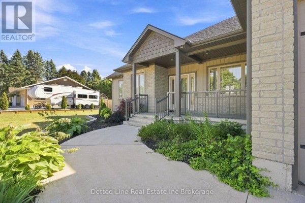 The front entrance of a beige brick bungalow with a covered porch and lush landscaping. - 3677 59 Highway, Norfolk