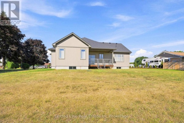 The backyard of a beige bungalow with a wooden deck and a large, dry grass lawn. - 3677 59 Highway, Norfolk