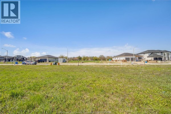 Wide shot of a grassy undeveloped lot with new homes and construction sites in the background. - 3679 Farrow Avenue, Windsor
